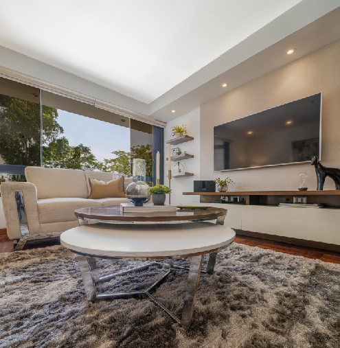 Modern living room with custom TV wall, large window, layered coffee tables, and neutral seating
