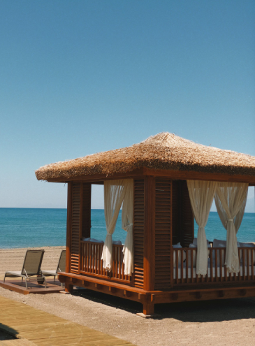 Waterfront cabana addition with thatched roof, lounge area, and beachfront outdoor living space