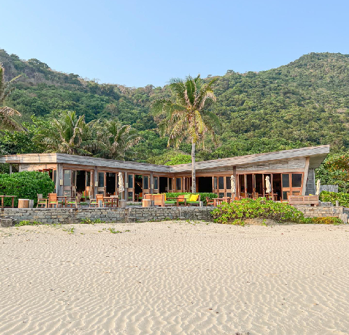 Waterfront home addition with beachfront outdoor living space, patio seating, and coastal landscaping