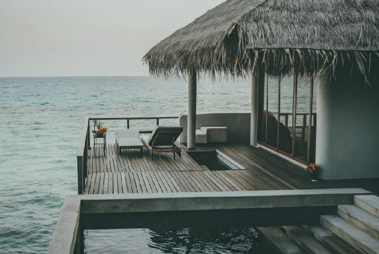 Waterfront home addition with private deck, lounge seating, thatched roof, and ocean view