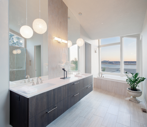 Contemporary bathroom renovation featuring a double vanity, modern lighting, soaking tub, and waterfront view through large windows.