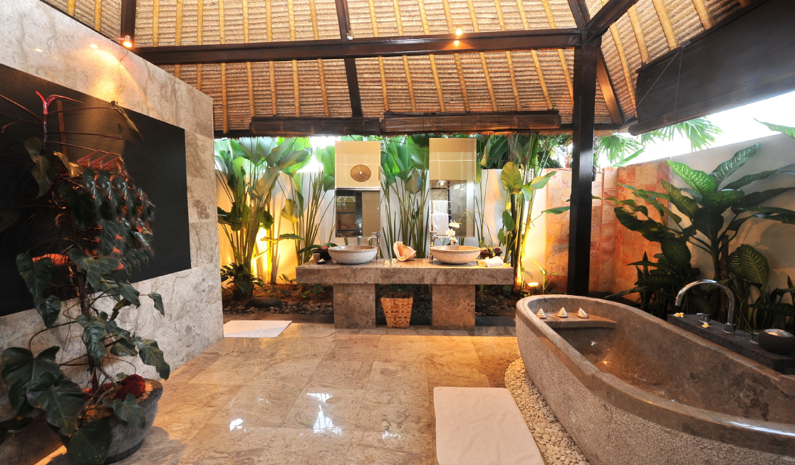 Luxury spa-style bathroom remodel featuring a natural stone soaking tub, tropical landscaping, dual vanities, and an open-air design.