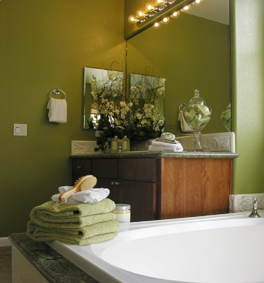 Traditional bathroom remodel featuring a custom wood vanity, decorative mirror, green accent walls, and elegant bathroom finishes.